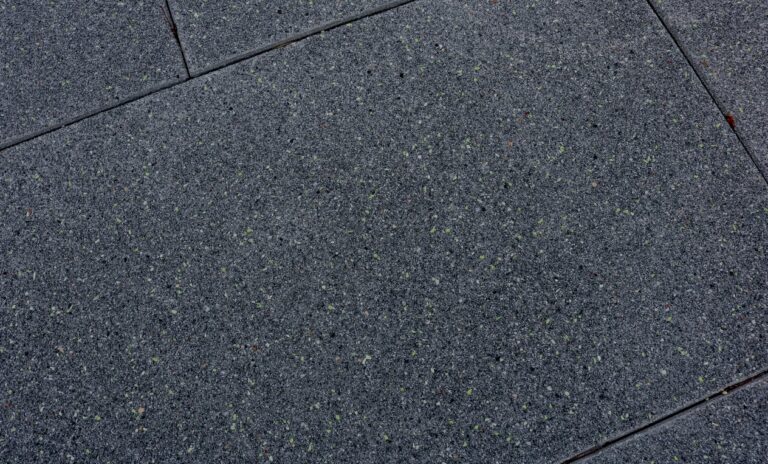 Close-up texture view of a dark gray architectural plaza paver featuring a speckled, reflective aggregate finish and clean joint lines.