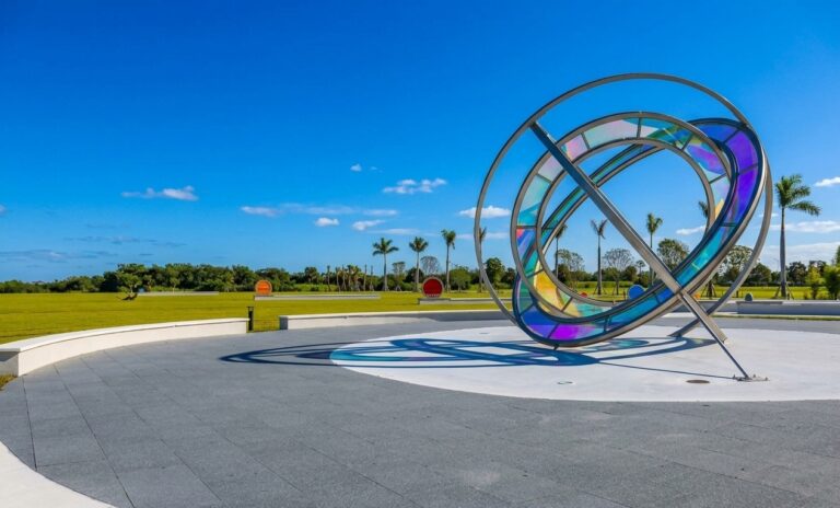 Side view of the large Celestial Plaza sundial sculpture showcasing the custom dark gray paving field, white concrete borders, and distant park lawn infrastructure.