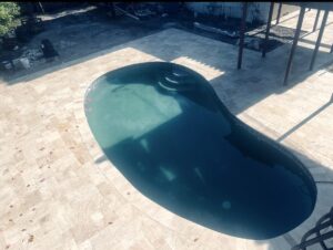 Kidney-shaped swimming pool surrounded by beige tile patio, with built-in steps and long shadows over the water.