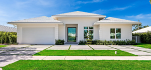 Modern white stucco house in Delray Beach featuring a custom concrete grid driveway with embedded grass strips, a two-car garage, and a glass entry door under a bright blue sky.