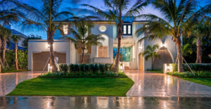 Upscale coastal home illuminated at night, highlighting a beautifully curved, high-gloss brick paver driveway and pristine green lawn by Cobra Construction.